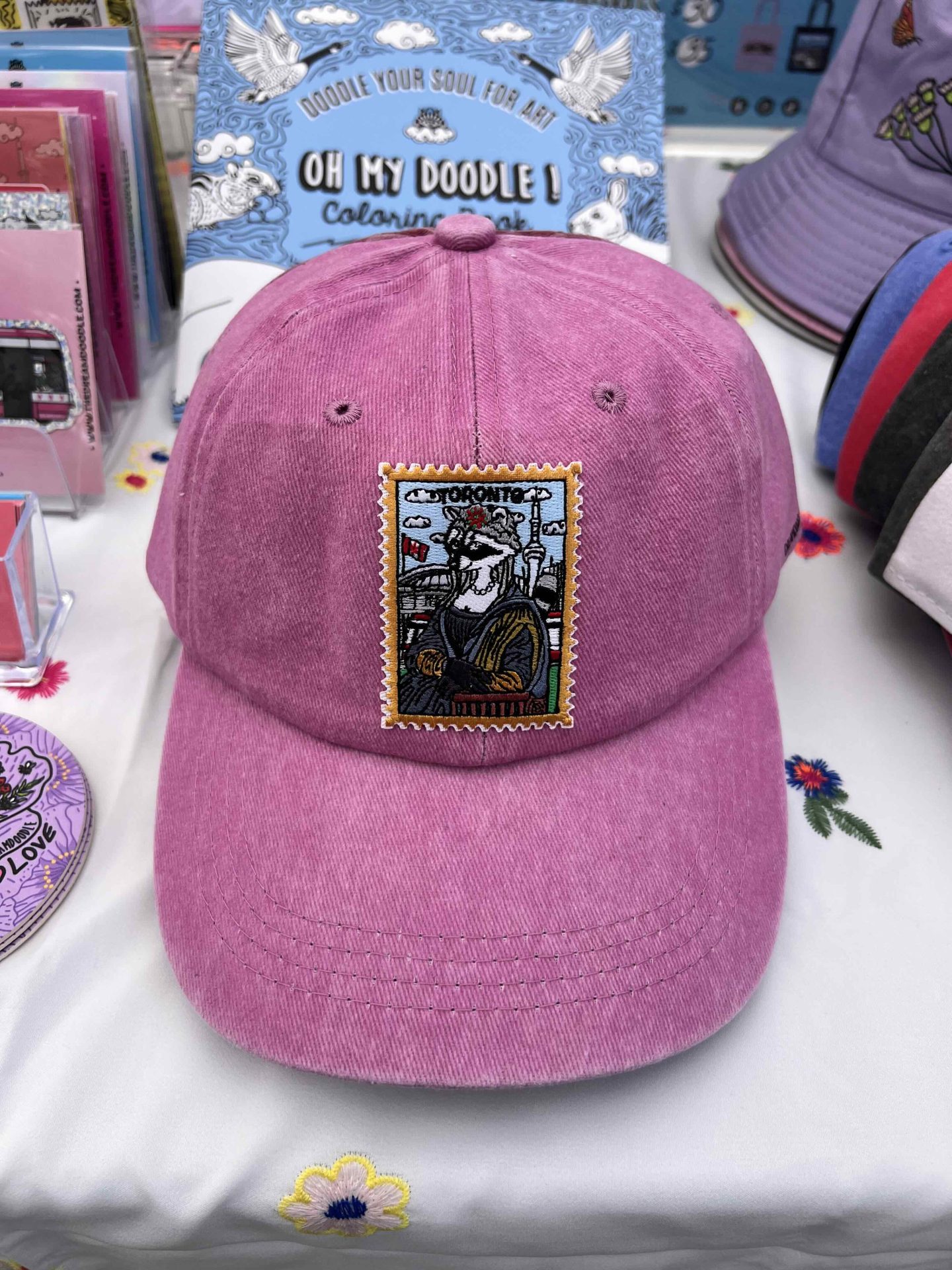 A Dreamdoodle Toronto Mona Lisa raccoon embroidered patch on a pink baseball cap